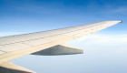 airplane wing against blue sky with faint clouds in distance 
