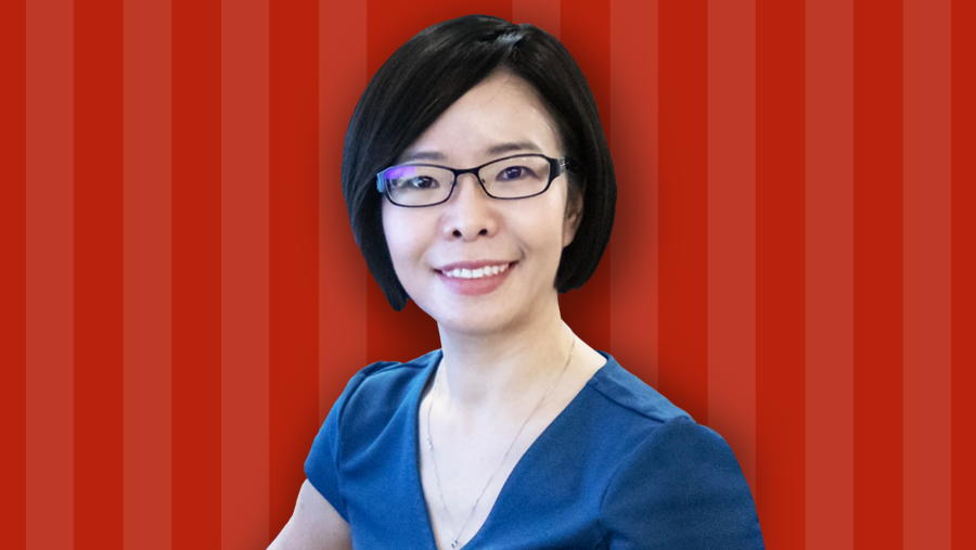A woman in black glasses and a blue shirt in front of a red striped background 