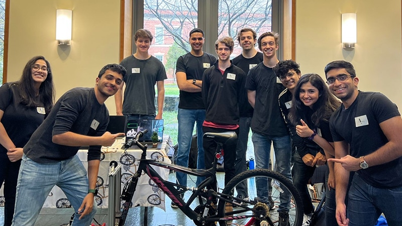 A group of students stand around a bicycle on a stand