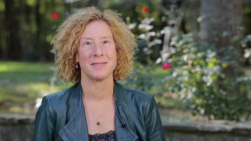 Cate Brinson sitting in front of stone wall with greenery in background