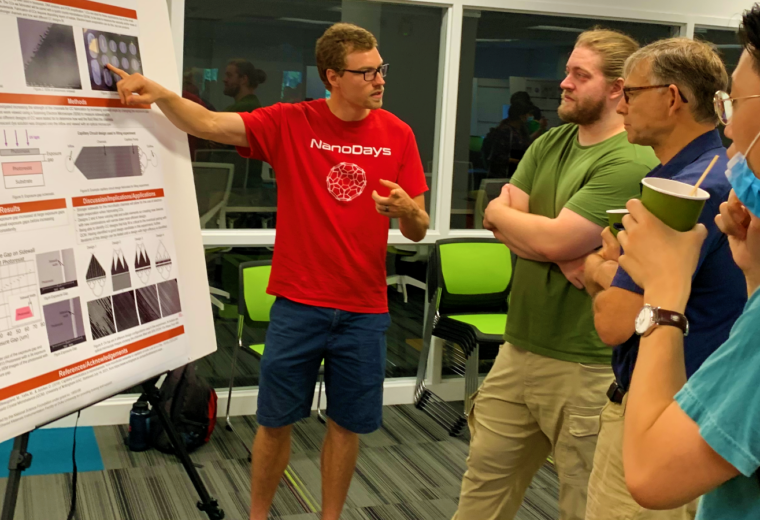 three people listen to a fourth person pointing at a research poster