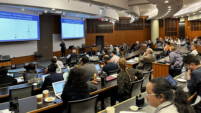 a crowded conference room with a speaker standing between two screens