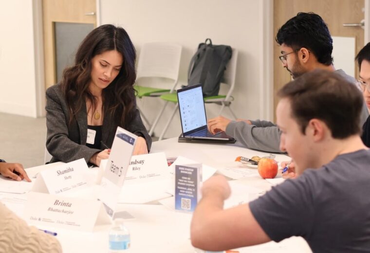 a woman and two men work at a big round table with computers