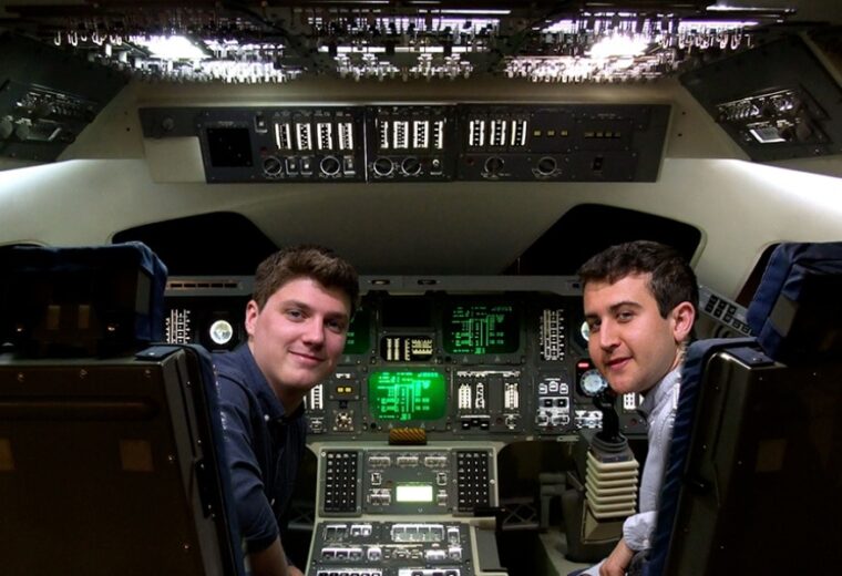 two male undergraduate students sitting in cockpit of space vehicle