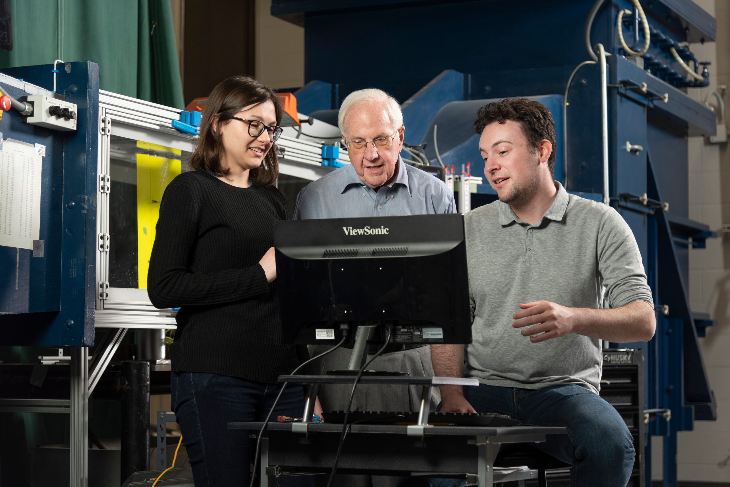 Students, professor look at a computer screen connected to an experimental wind tunnel