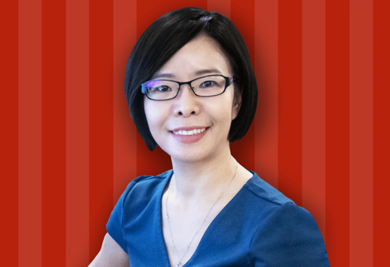 A woman in black glasses and a blue shirt in front of a red striped background