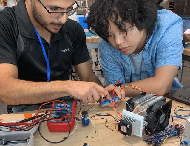 two people work at a bench on an electronics project