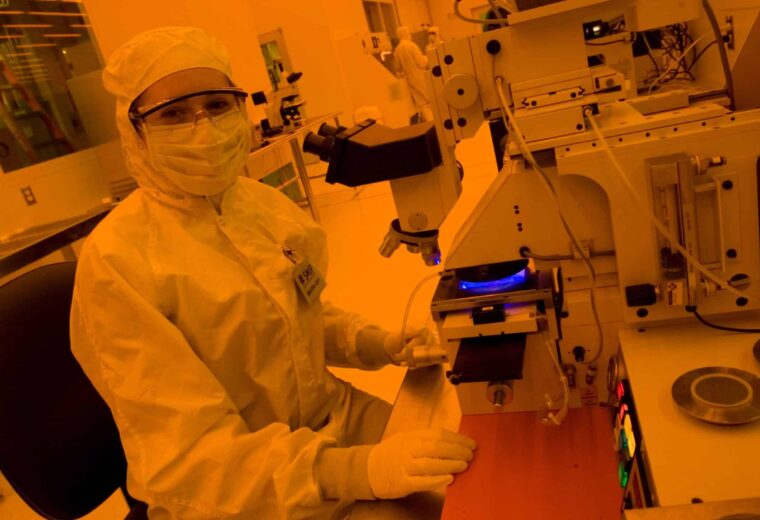 female student in clean room suit at microscope