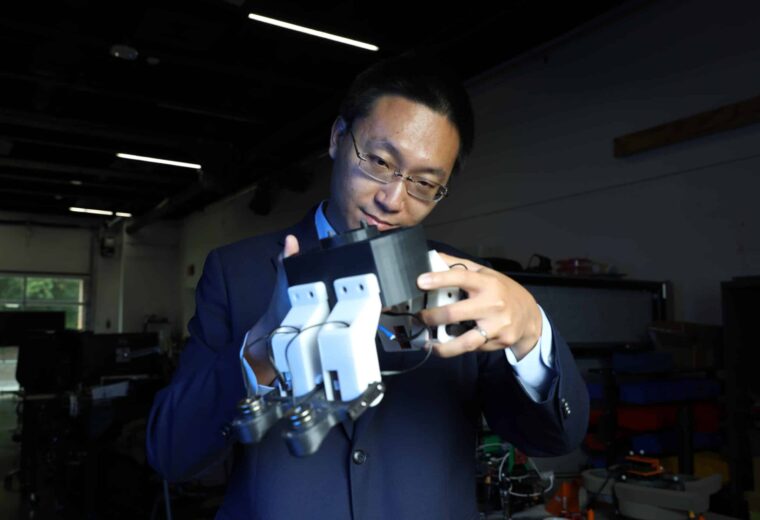 Man with glasses holding up and examining a four-legged white robot body.